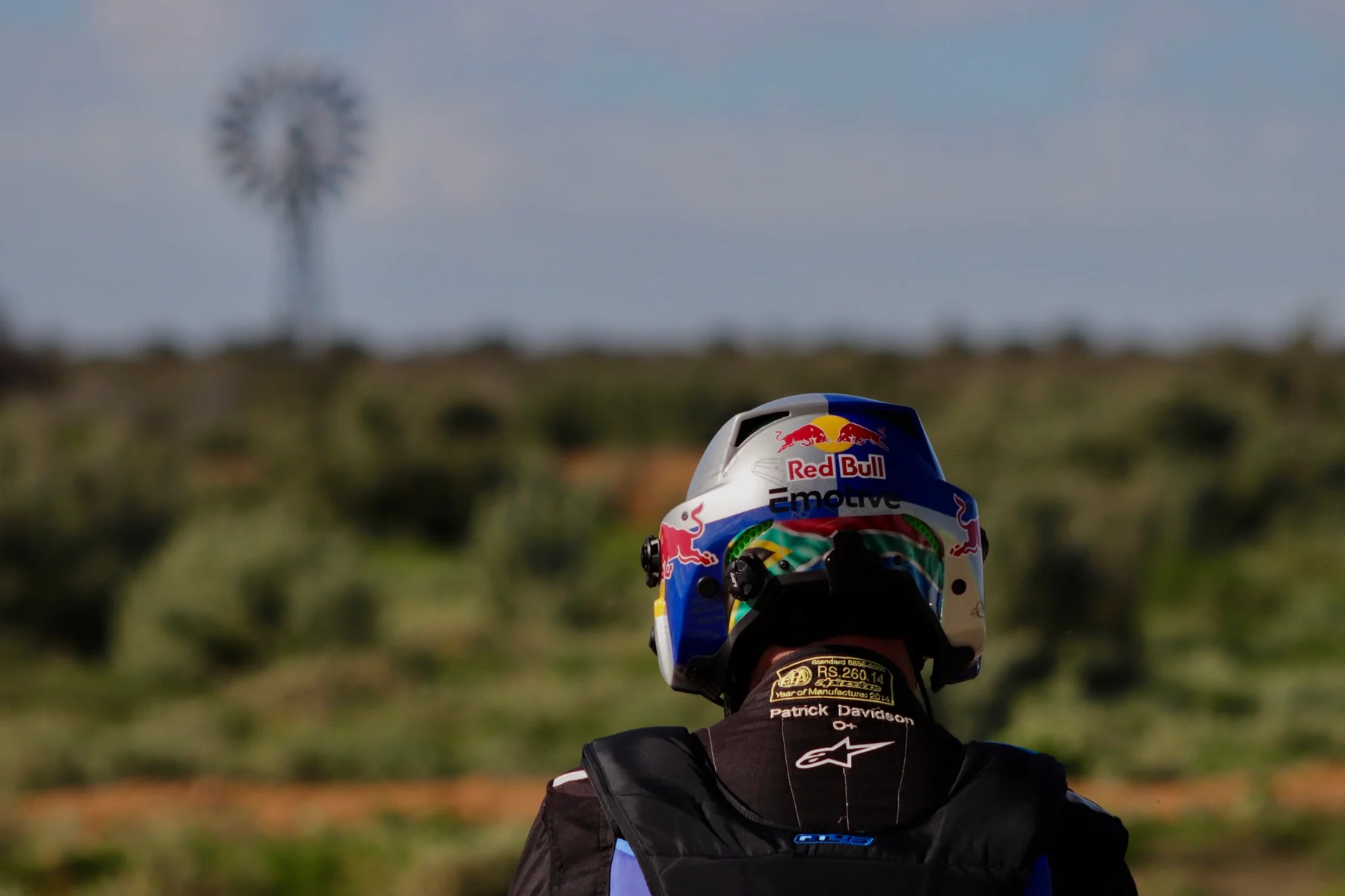 Patrick seen from behind wearing his Red Bull helmet with a Karoo windmill in the distance
